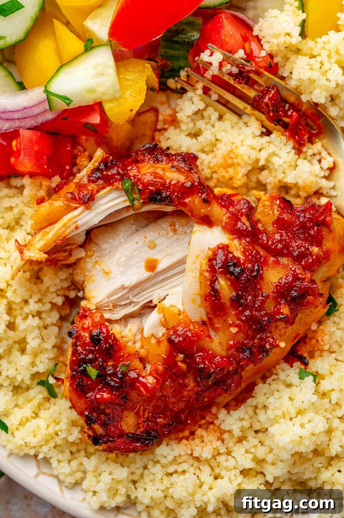 Shot of harissa chicken recipe plated with couscous. Fork has split the chicken showing the juicy, tender chicken.