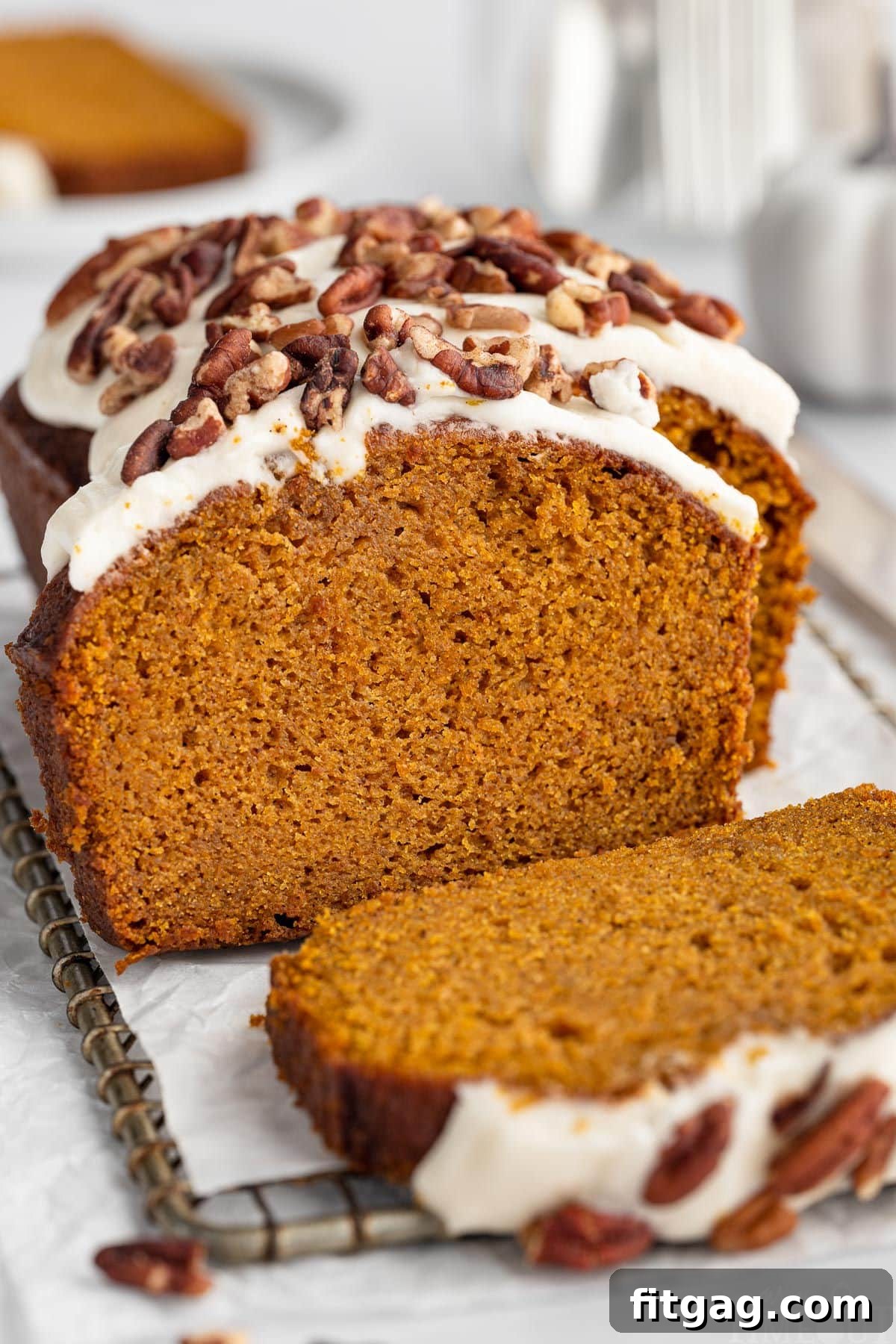 Easy pumpkin bread loaf sitting on cutting board with a few pieces sliced off. Loaf is topped with cream cheese frosting and pecans.