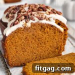 Easy pumpkin bread loaf sitting on cutting board with a few pieces sliced off. Loaf is topped with cream cheese frosting and pecans.