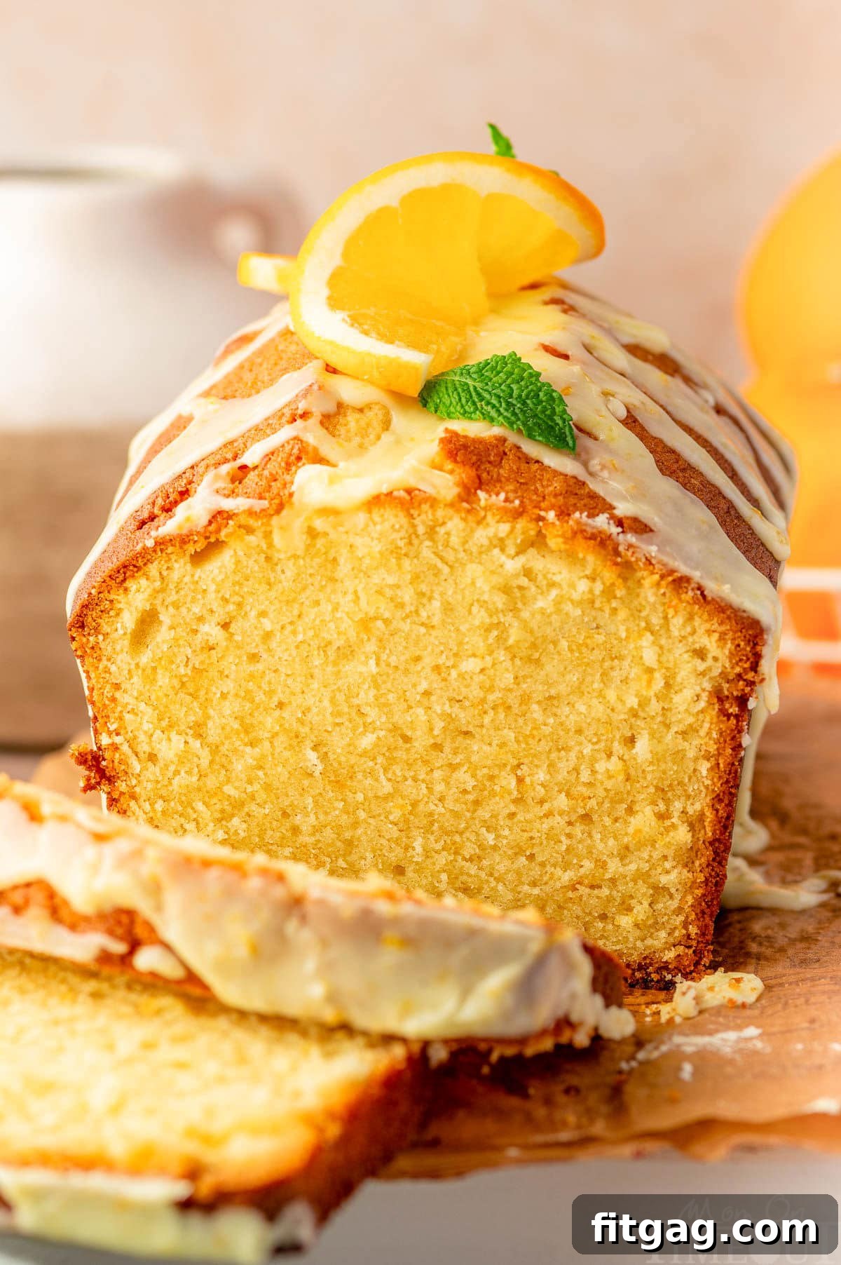 A front view of a perfectly baked and glazed Orange Pound Cake, with two slices already removed, on a wooden cutting board.
