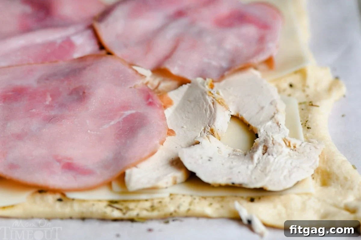A close-up shot showcasing the beautiful layers of crescent dough, Swiss cheese, thinly sliced chicken, and ham before rolling.