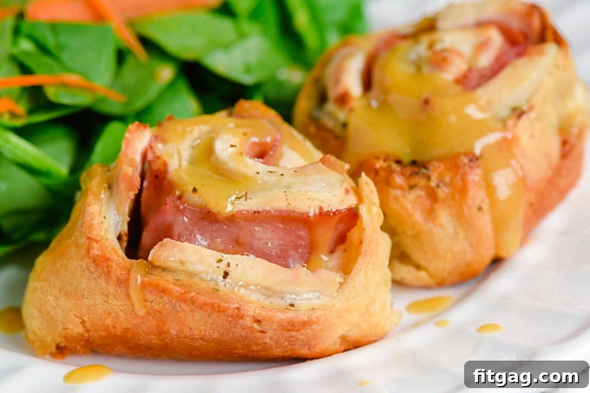 A plate featuring Chicken Cordon Bleu Crescent Roll ups drizzled with Honey Dijon sauce, served alongside a fresh green salad.