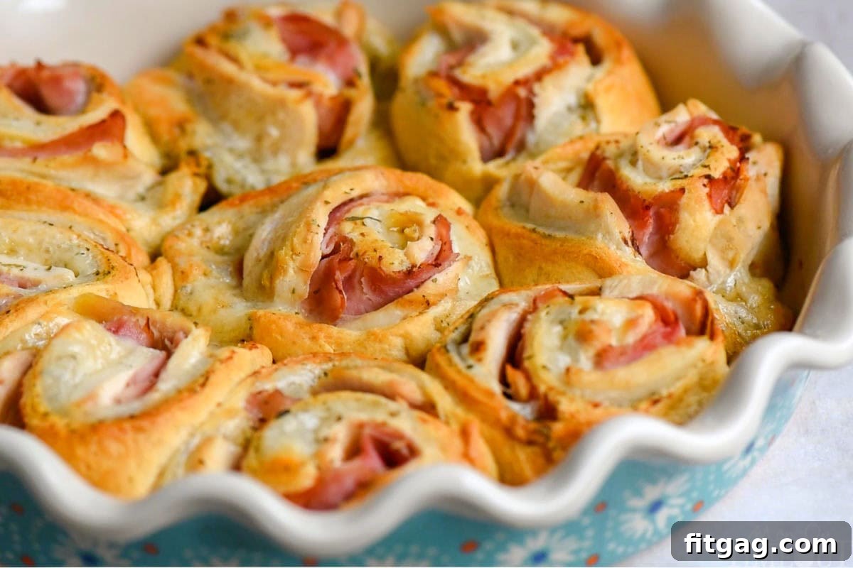 A wide shot of several golden brown Chicken Cordon Bleu Crescent Roll ups artfully arranged in a white ceramic pie dish.