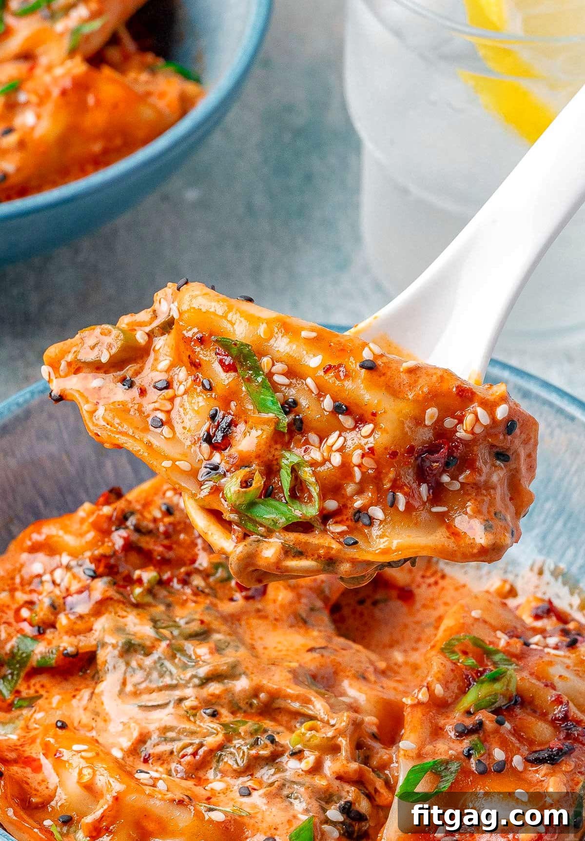 A perfectly cooked chicken dumpling being lifted by a spoon from a bowl brimming with creamy baked dumplings, highlighting its tender texture.