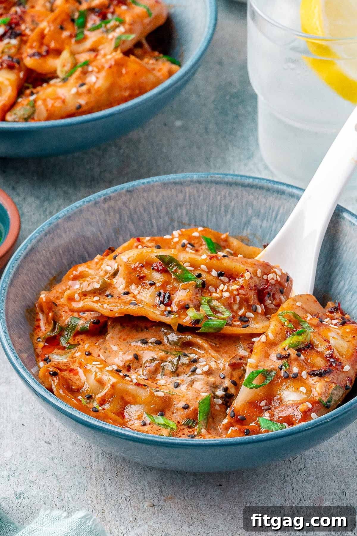 A beautifully presented bowl of baked dumplings, artfully garnished with vibrant green onions, a sprinkle of sesame seeds, and a delightful swirl of chili crisp, ready to be savored.