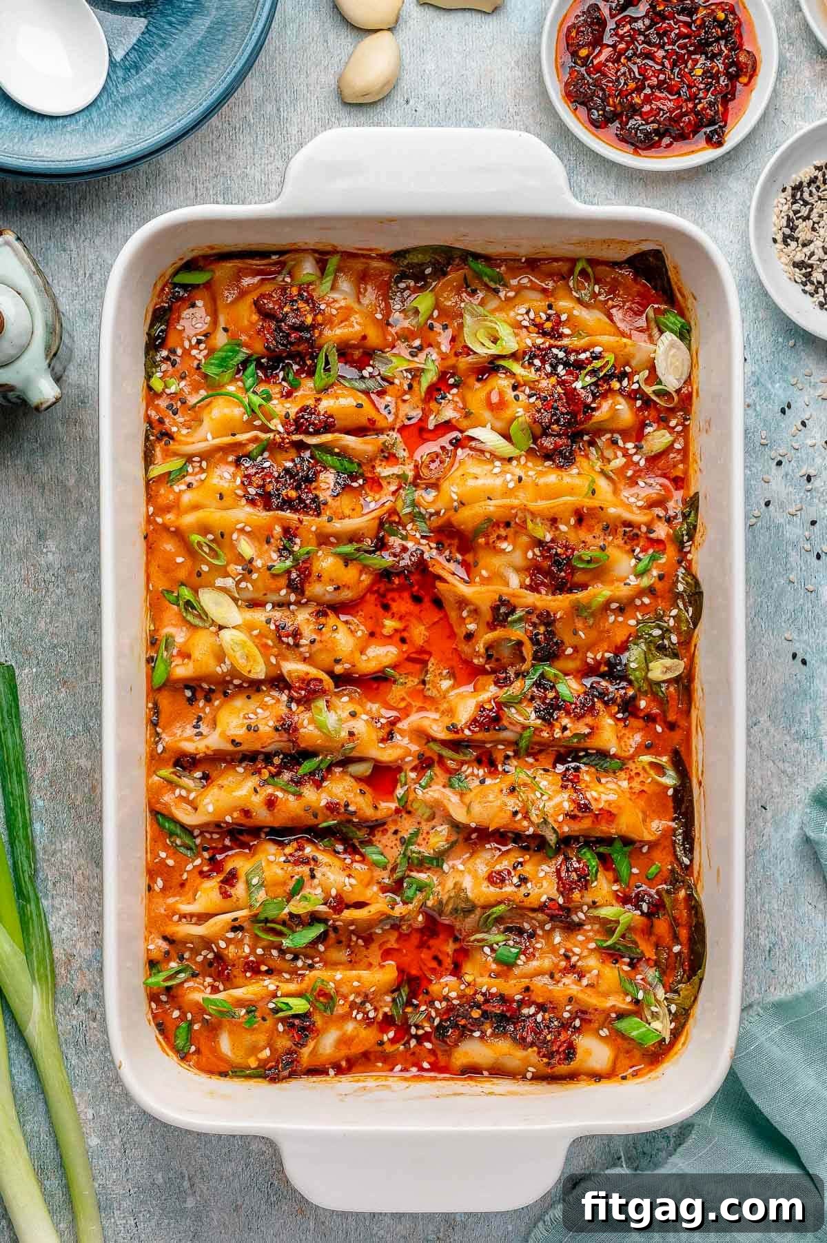 Overhead shot of viral baked dumplings in white baking dish topped with chili crips, green onions and black and white sesame seeds. Spoon in dish ready to serve the dumplings.