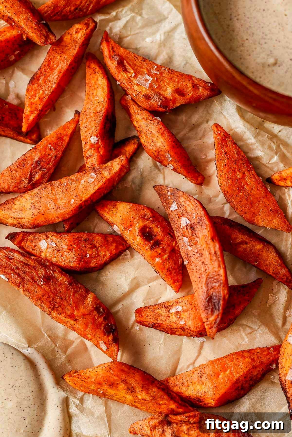 Overhead shot of perfectly roasted sweet potato wedges on a baking sheet lined with parchment paper, lightly sprinkled with sea salt.