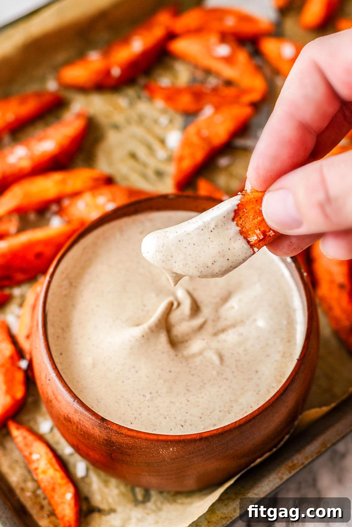 A sweet potato wedge being dipped into a bowl of creamy cinnamon marshmallow dipping sauce, highlighting the delicious pairing.