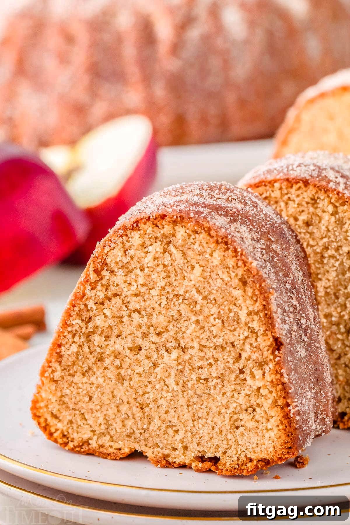 A perfectly sliced piece of homemade apple cider donut cake, showcasing its moist texture and cinnamon-sugar topping, resting on a round white plate with more slices visible in the background, ready to be enjoyed.