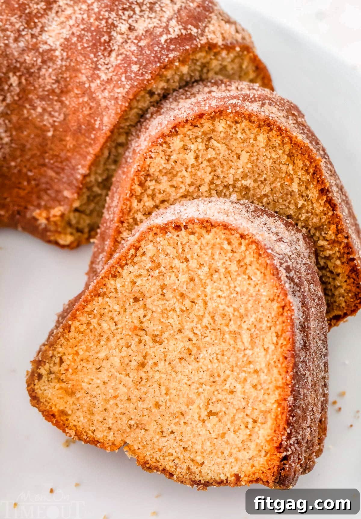 An inviting angled-down view of two generously cut pieces of apple cider bundt cake, freshly removed from the larger bundt and gently resting on a pristine white cake stand, ready to be enjoyed.
