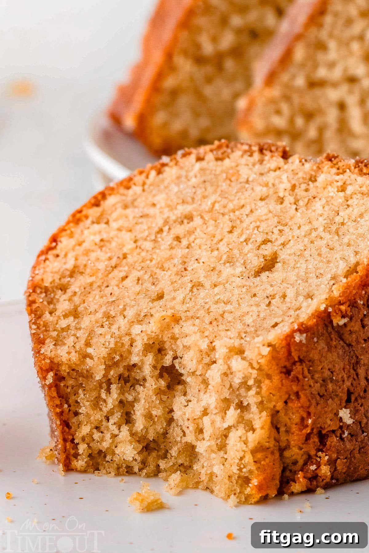 A close-up of a single slice of apple cider donut bundt cake on a white plate, with a bite playfully taken out, revealing its moist and tender interior. This enticing shot highlights the cake's deliciousness.