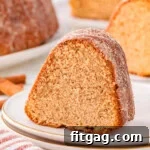 Piece of apple cider donut cake on round white plate. More pieces can be seen in the background.