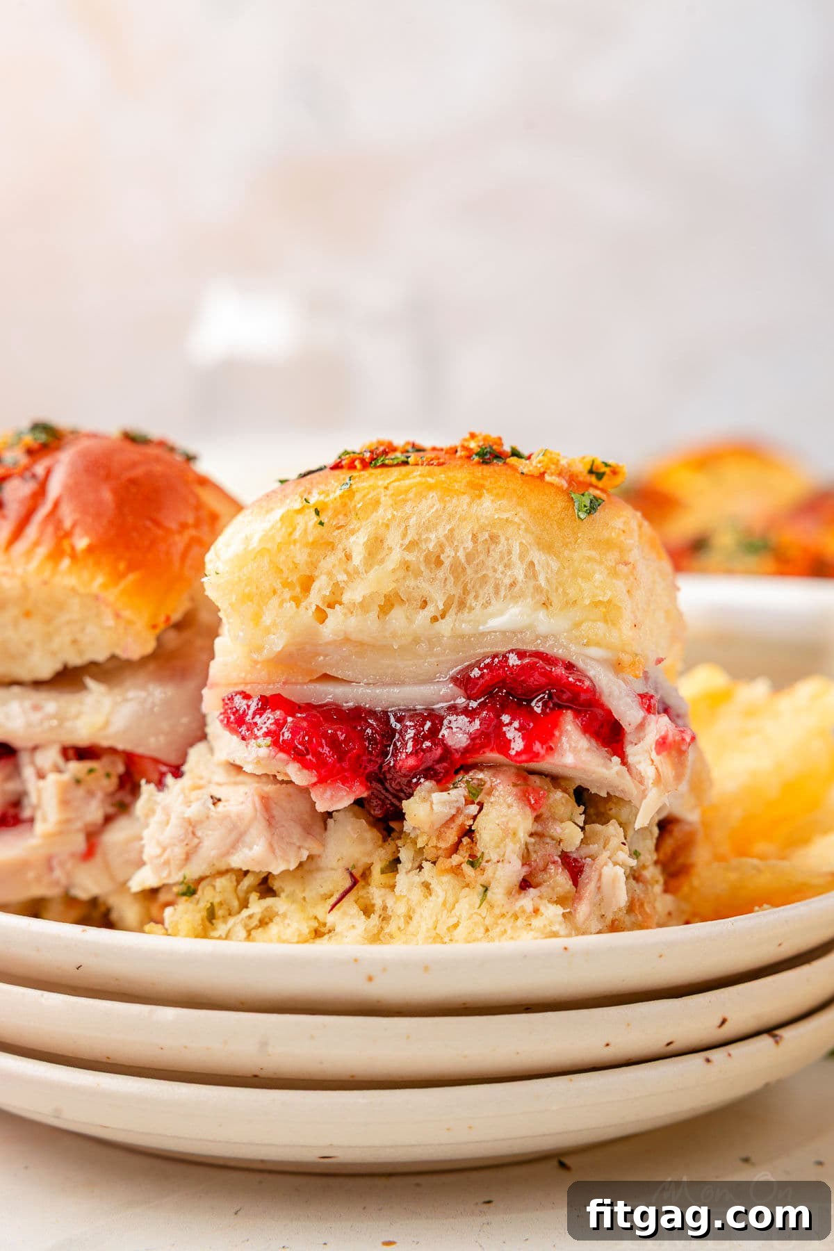 Petite Turkey Stacks 2 Two Turkey sliders sitting on small round plates stacked three high. Cranberry sauce, juicy turkey, and stuffing can all be seen in between the soft hawaiian roll.