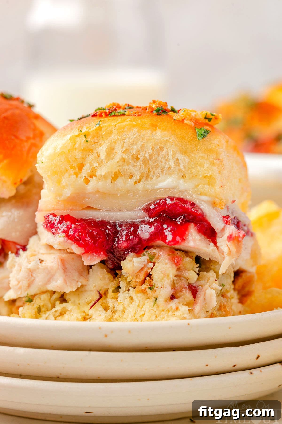 Petite Turkey Stacks 7 Turkey slider sitting on small round plates stacked three high. Cranberry sauce, juicy turkey, and stuffing can all be seen in between the soft hawaiian roll.