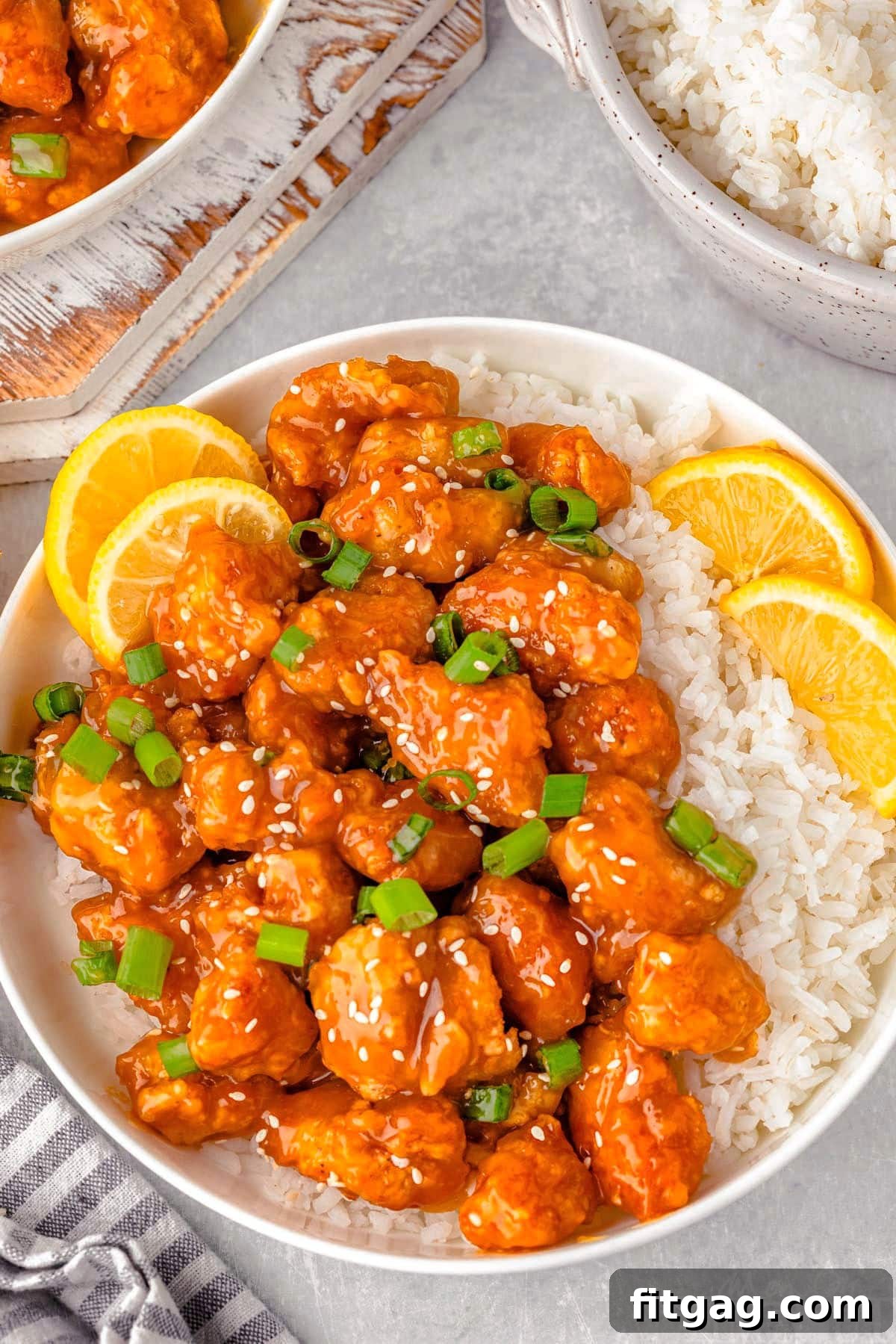 Overhead shot of lemon chicken and white rice on round plate with lime slices and green onions for garnish.