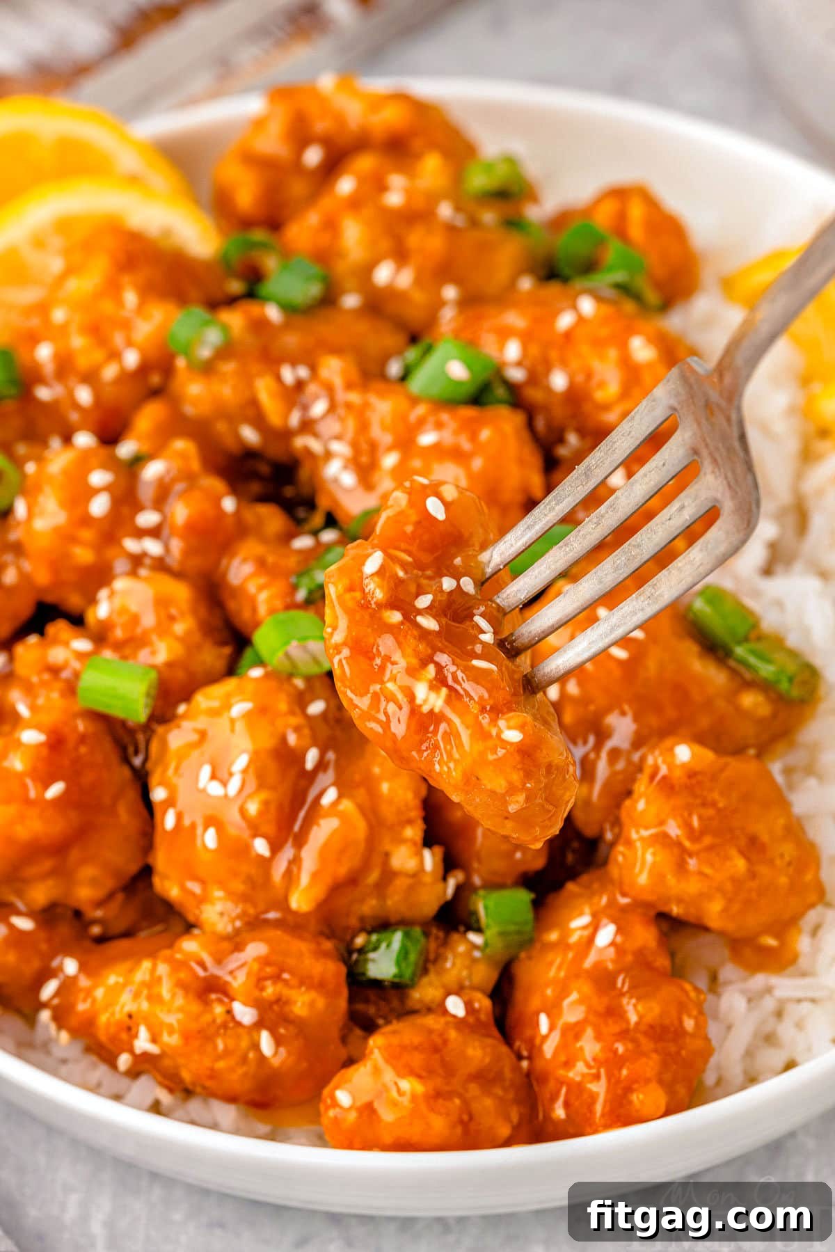 Golden Glazed Lemon Chicken 6 Bite of lemon chicken chinese on fork being lifted away from plate of chinese lemon chicken.