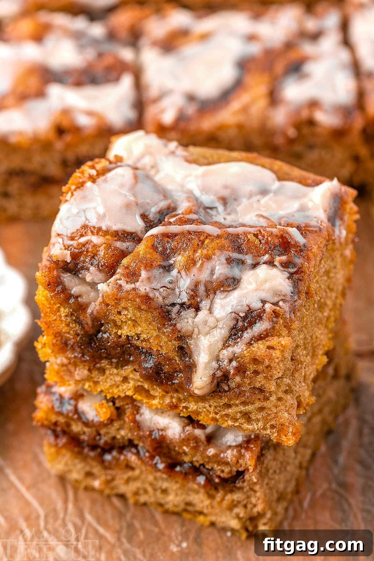 Two pieces of cinnamon roll pumpkin focaccia stacked on a wood surface with more focaccia in the background.