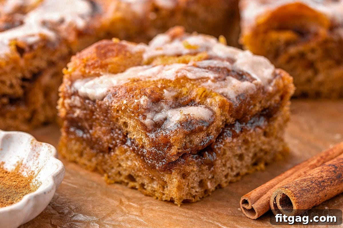 Wide shot of pumpkin focaccia cinnamon roll on brown parchment next to cinnamon stick. 
