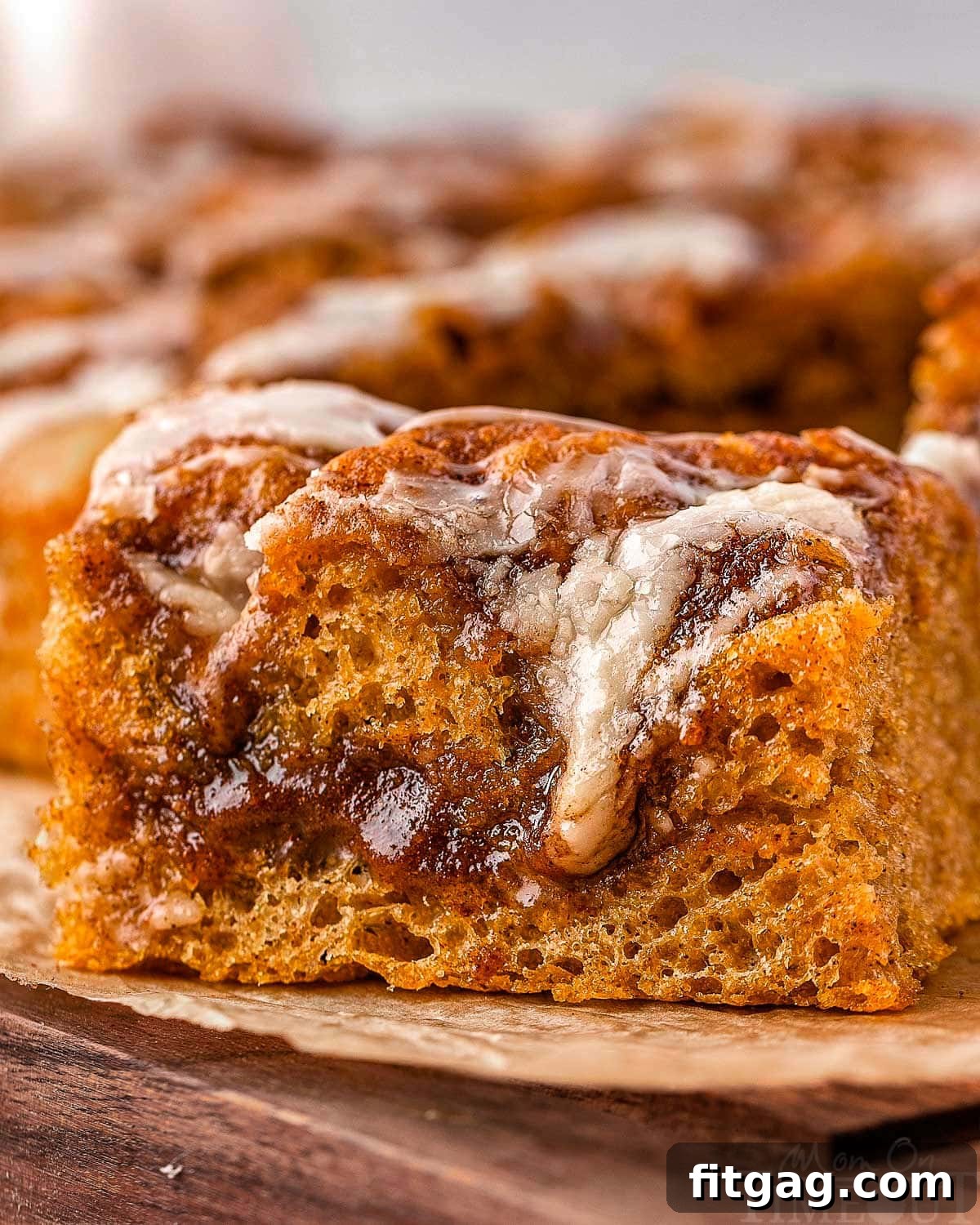 Piece of pumpkin cinnamon roll focaccia sitting on brown parchment on a wood cutting board. 