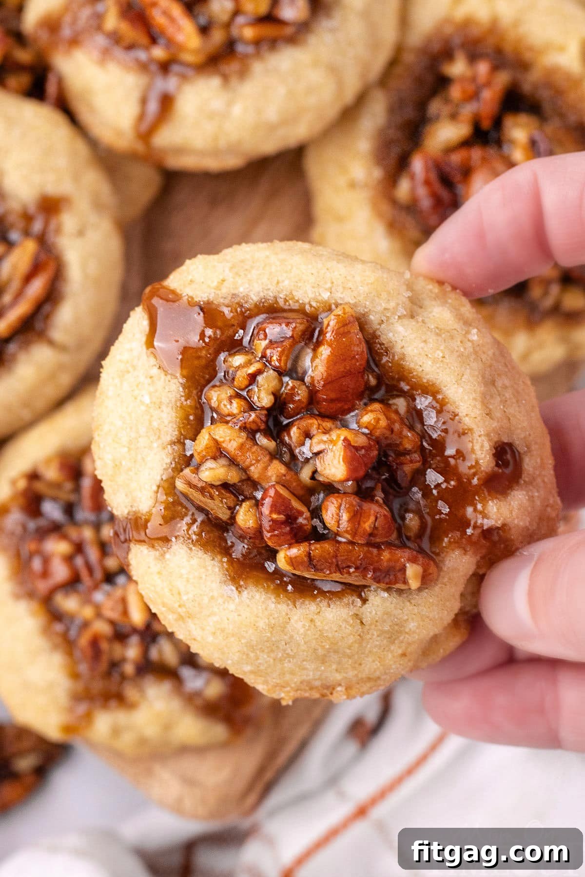 Pecan pie thumbprint cookies lifted off the board with a hand.