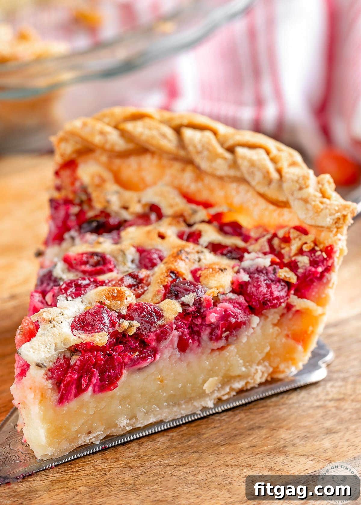 A perfectly baked slice of Cranberry Custard Pie, showcasing its vibrant red cranberry layer and creamy golden custard, resting on a rustic wooden cutting board.