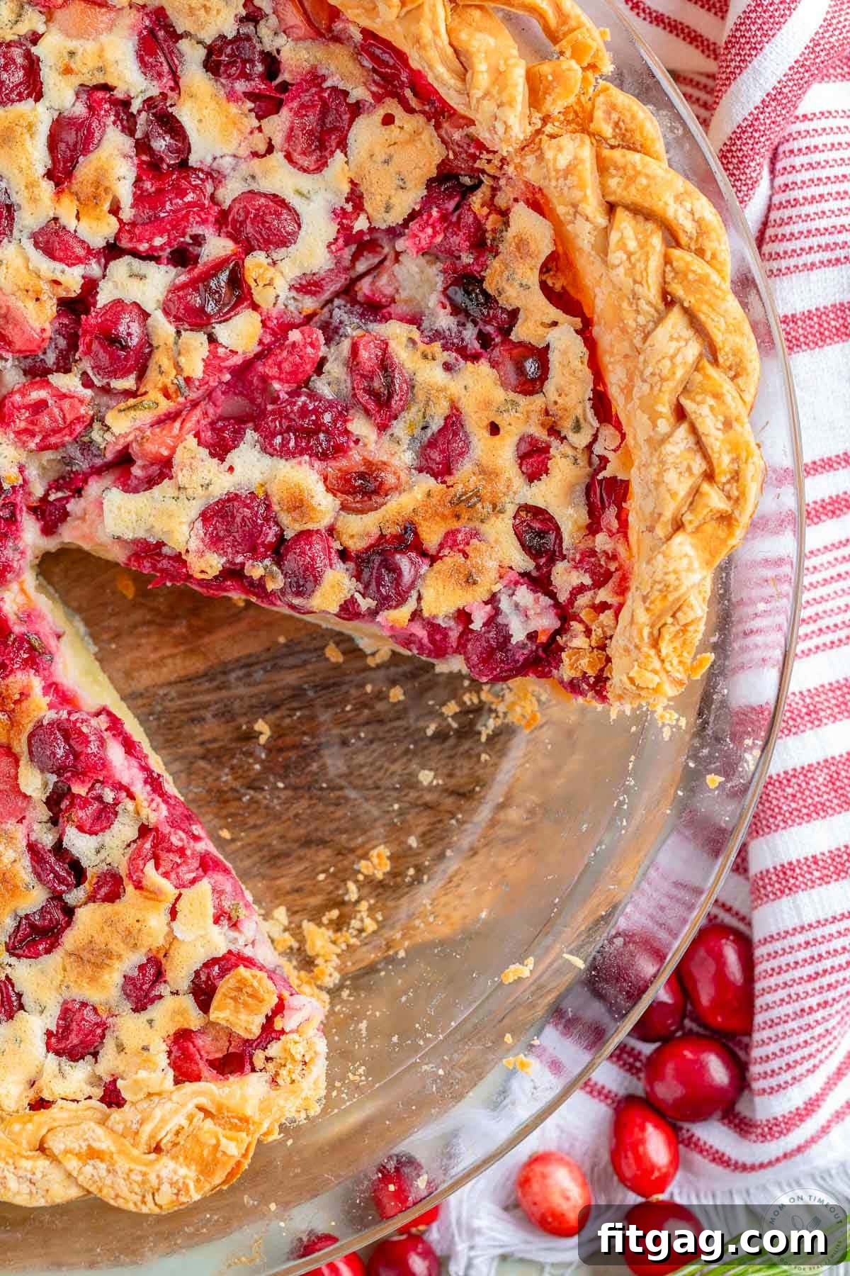 An overhead shot of a freshly baked Cranberry Custard Pie in a glass pie plate, with one slice perfectly removed, revealing the layers of fruit and custard.