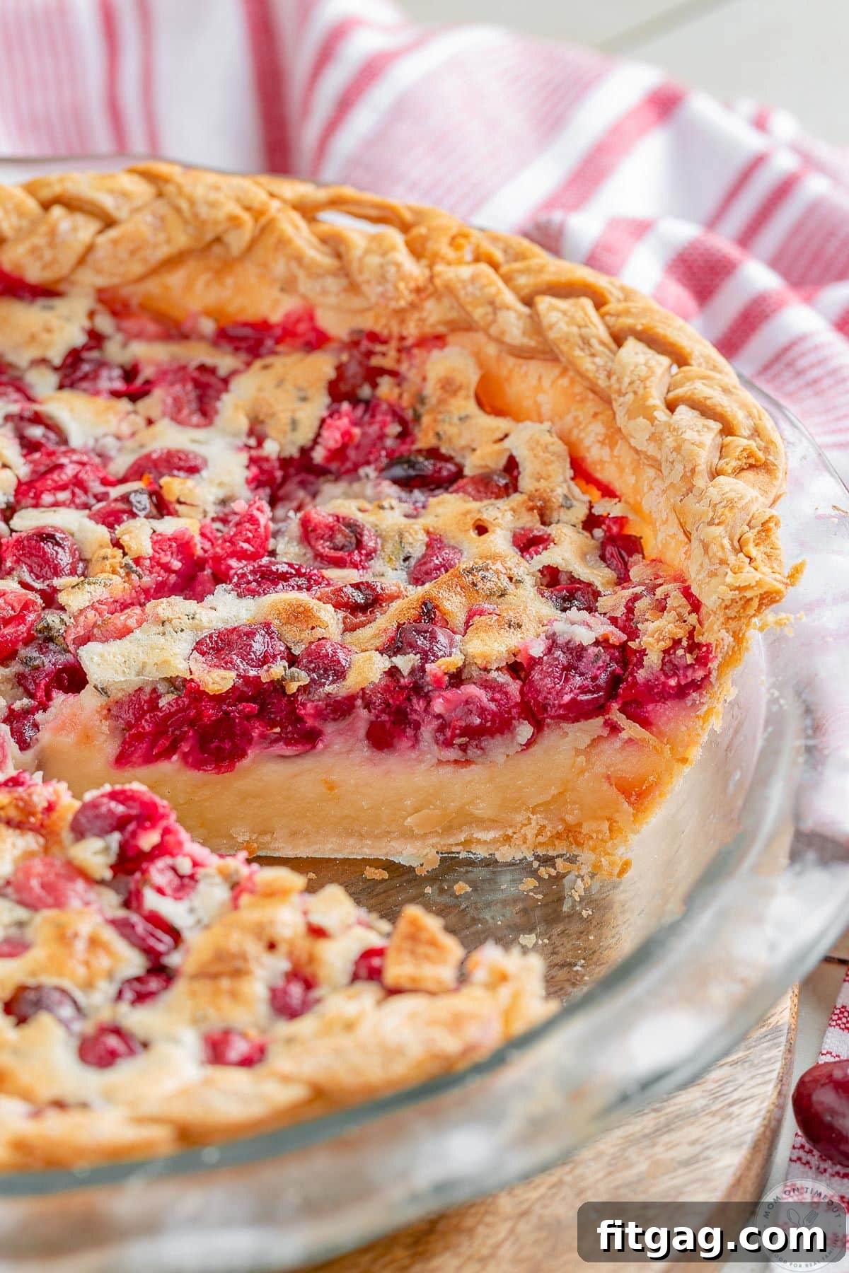 An angled overhead view of a whole Cranberry Custard Pie in a glass pie plate, showcasing its golden crust and glistening cranberry-studded custard.