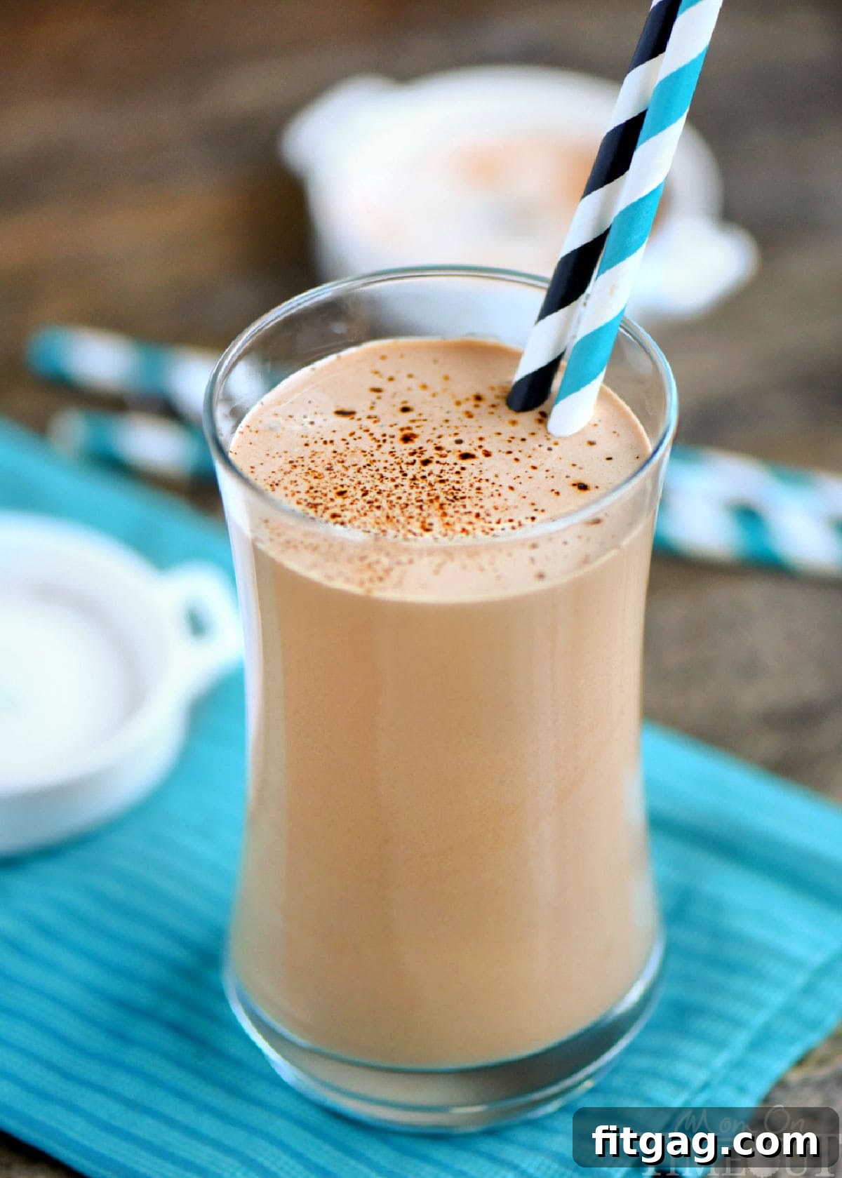 Espresso Power Shake 2 Coffee protein shake in a tall glass with two paper straws. Glass is sitting on teal napkin on a wood surface.