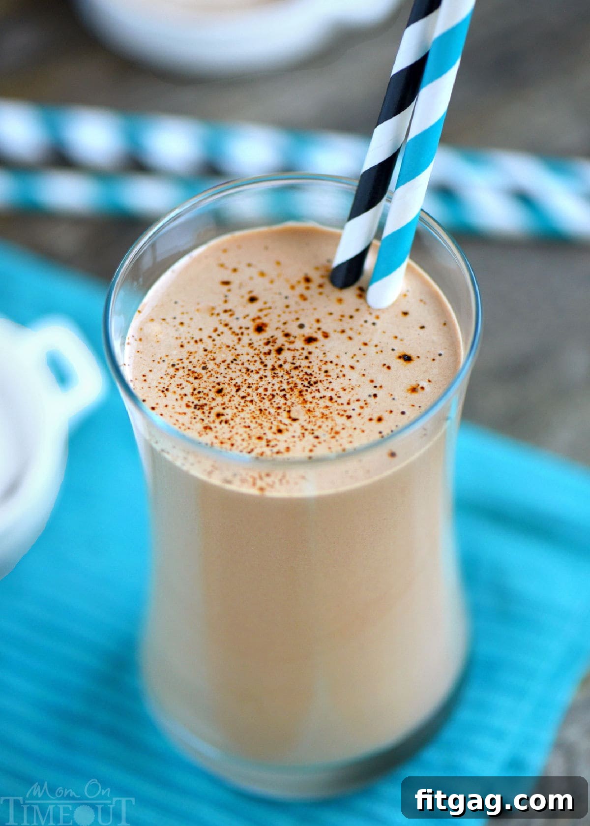 Espresso Power Shake 3 Angled top down view of protein and coffee shake poured into a tall glass and finished off with a dusting of espresso powder. Shake is resting on a striped teal towel in front of a few straws.