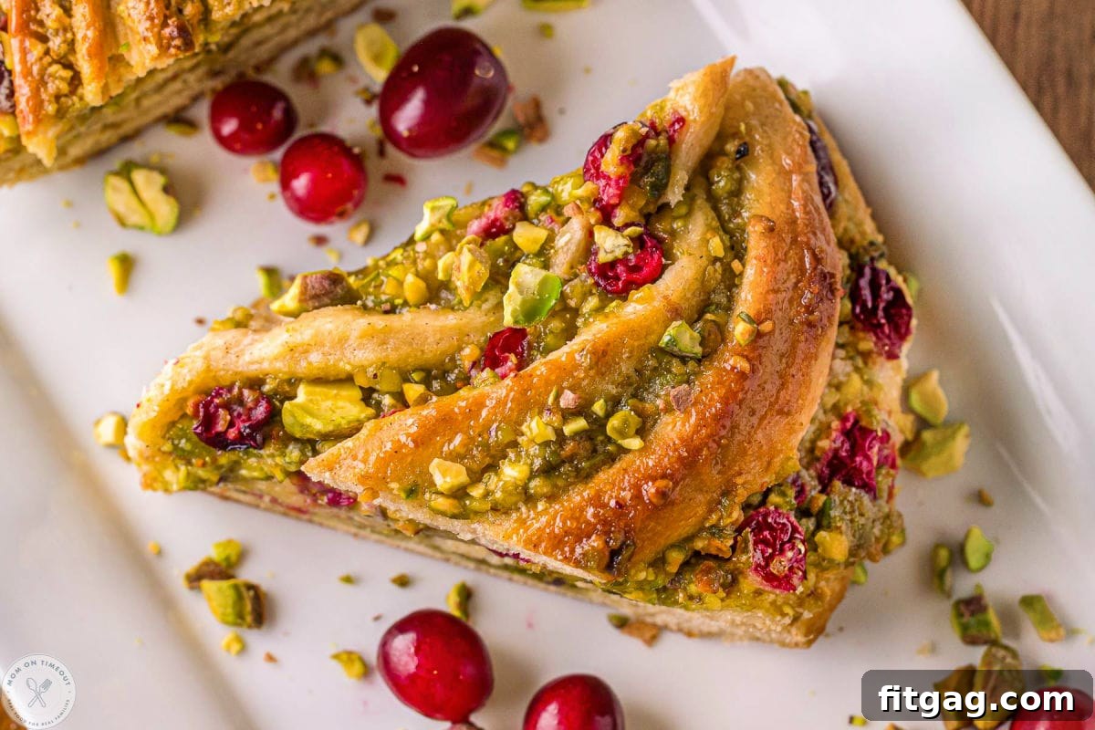 Wide shot of piece of babka bread on white tray. Shown with cranberries and pistachios.