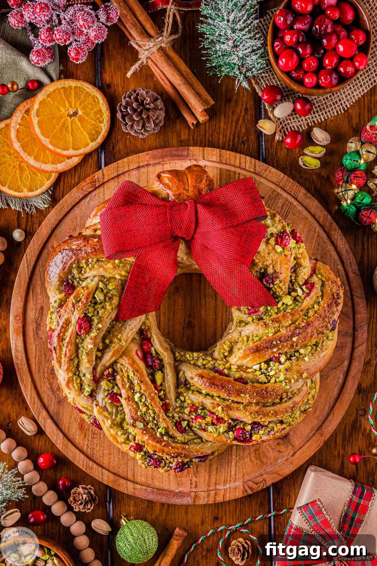 Overhead shot of cranberry pistachio babka shaped as a wreath sitting on round wood board.