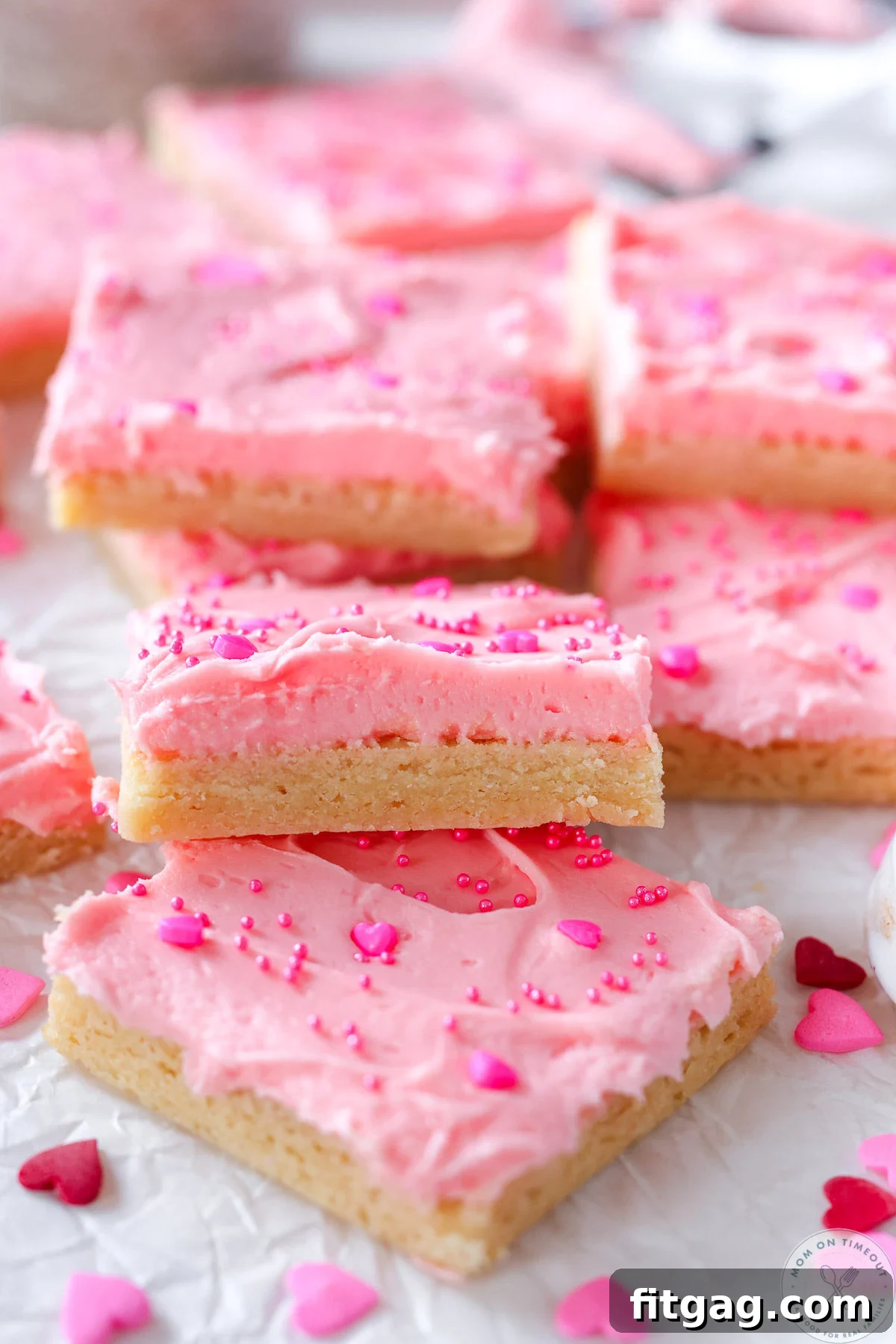 Love-Struck Sugar Cookie Squares 3 Sugar cookie bars laid out on white parchment. Bars have pink frosting and sprinkles.