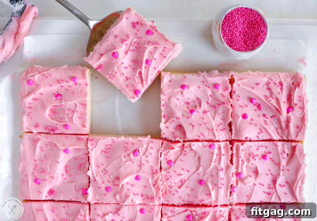 Sweetheart Sugar Cookie Bars 7 Valentine's Day Sugar Cookie Bars, perfectly cut into neat squares and arranged on white parchment paper, with one bar being gently lifted away to show its delightful texture.