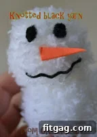 Image showing how to create eyes for a pom pom snowman by knotting black yarn