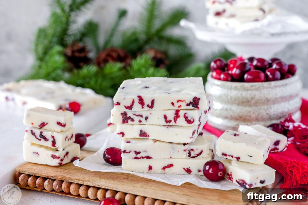 Wide shot of white chocolate cranberry fudge stacked on wood and marble cutting board with fresh cranberries off to the side.