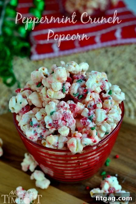 Close-up of freshly made Peppermint Crunch Popcorn in a vibrant red bowl, showcasing the generous coating of white chocolate and peppermint bits, with sprinkles adding a colorful touch.