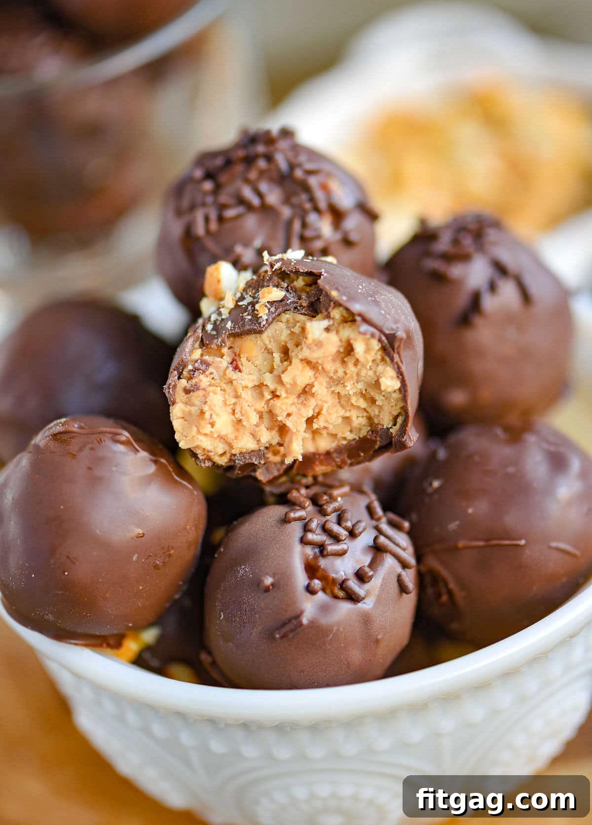 white glass bowl filled with peanut butter balls with rice krispies. each ball is topped with either chocolate jimmies or crushed peanuts.