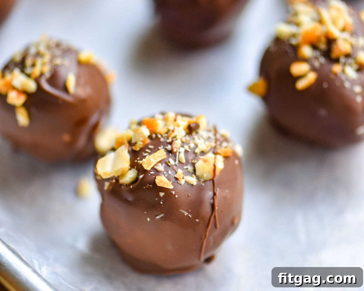 peanut butter balls covered in chocolate with crushed peanuts sprinkled on top sitting on a parchment lined baking sheet.