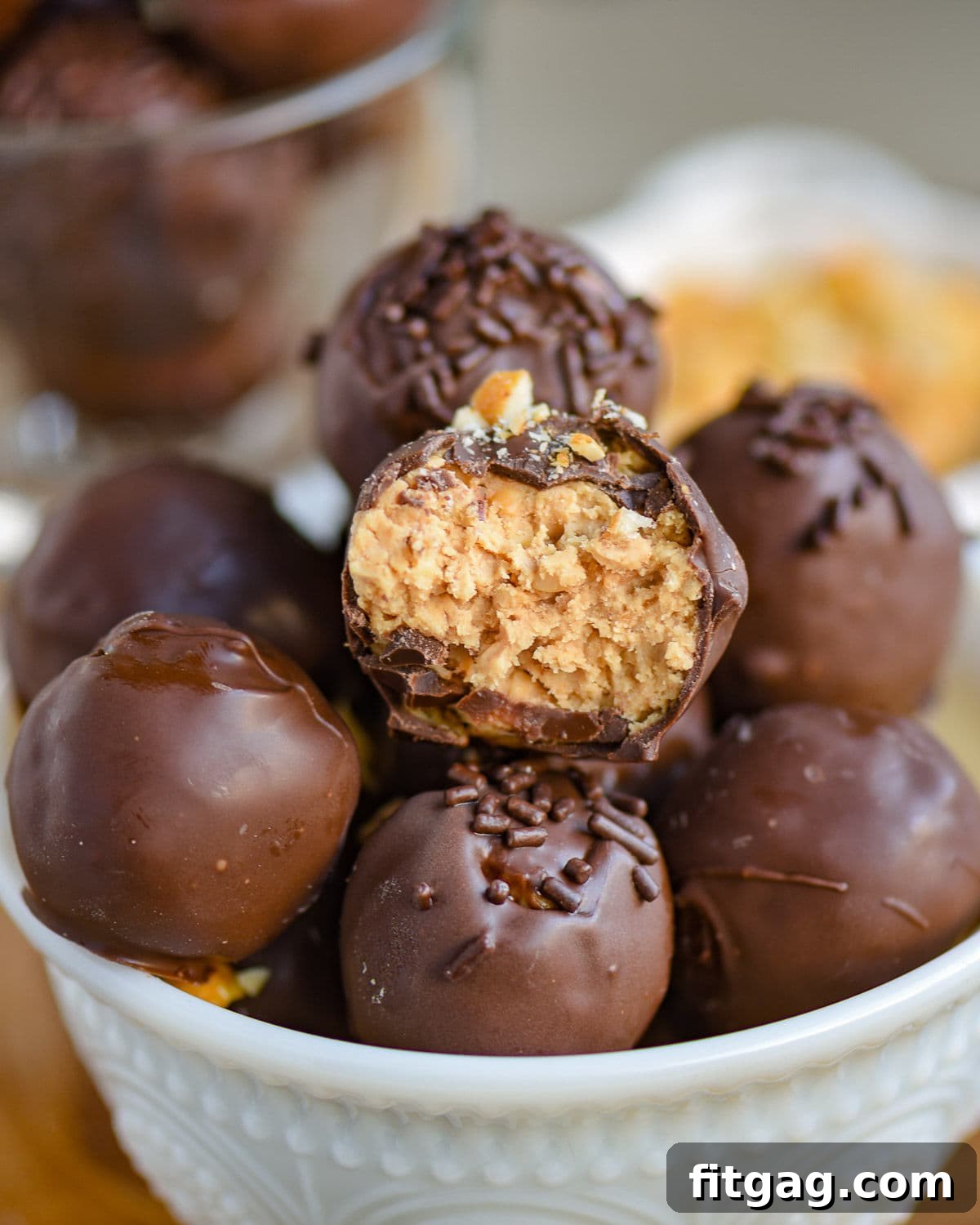 white glass bowl filled with peanut butter balls with rice krispies. each ball is topped with either chocolate jimmies or crushed peanuts.