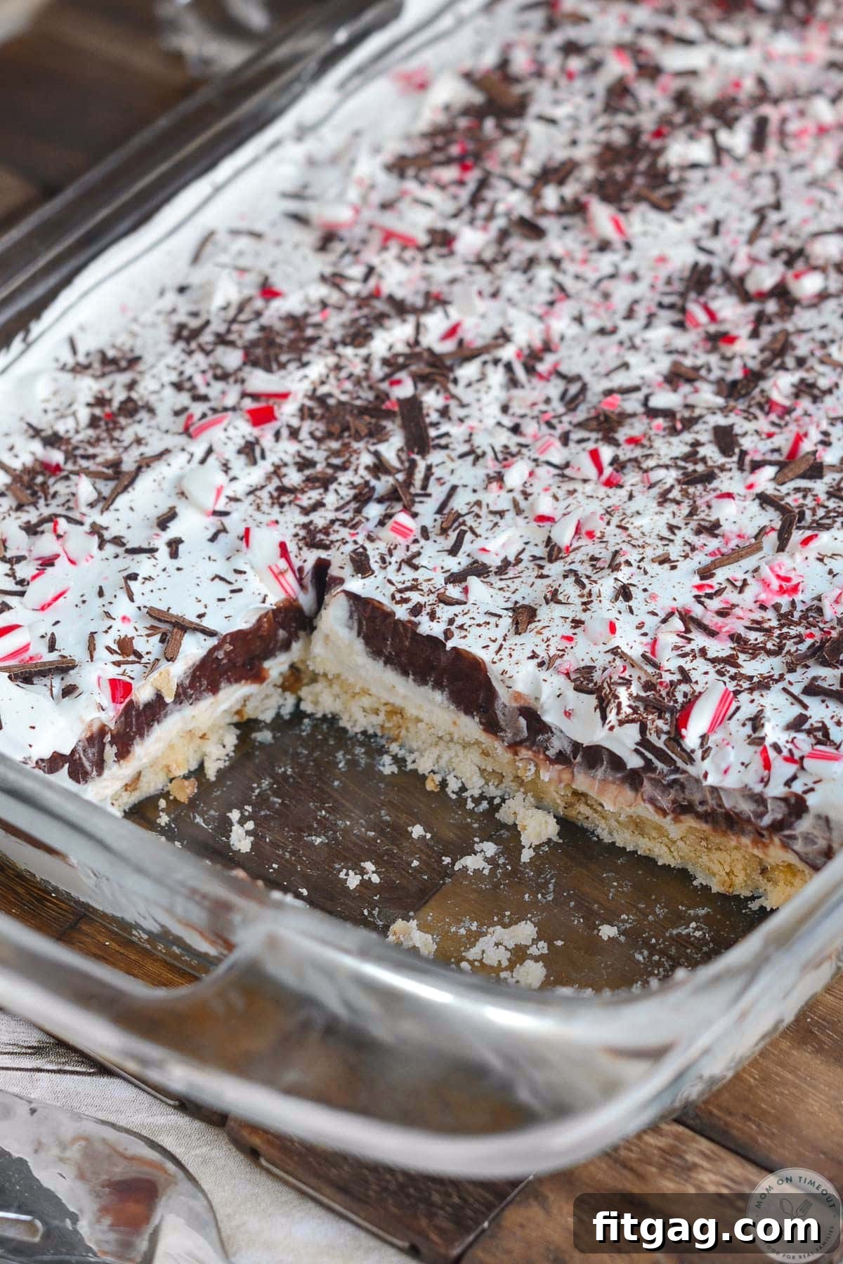 An overhead angled shot of a glass casserole dish filled with chocolate peppermint layered dessert, with a few servings already removed.