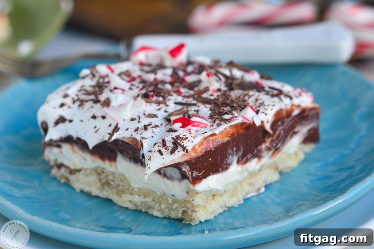 A four-layered chocolate peppermint dessert on a blue plate, topped generously with crushed candy canes. This Peppermint Lush is topped with crushed candy canes.