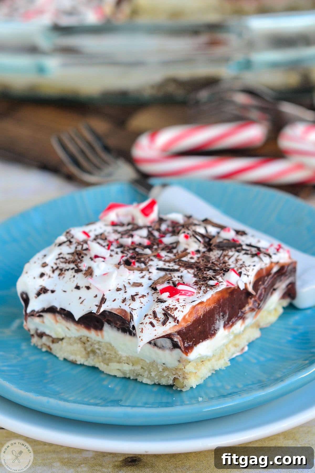 A four-layered chocolate peppermint dessert on a blue plate topped with candy canes. This Chocolate Peppermint 4 Layer Dessert is topped with crushed candy canes.