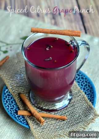 A festive glass of spiced citrus grape punch, garnished with orange slices and cranberries.