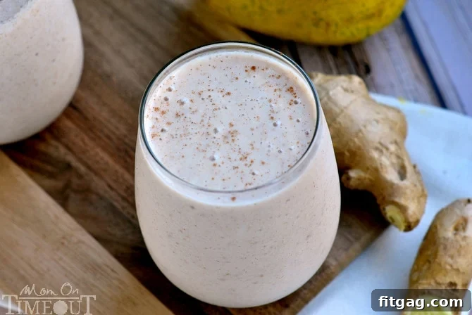 Wide view of a Pear Ginger Cinnamon Oat Smoothie in a short glass, next to fresh pear slices and ginger root on a wooden surface