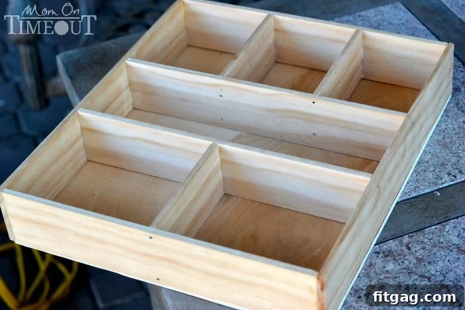 A plywood base with pencil lines tracing the outlines of compartments, guided by temporary divider placement, indicating where washi tape will be applied.