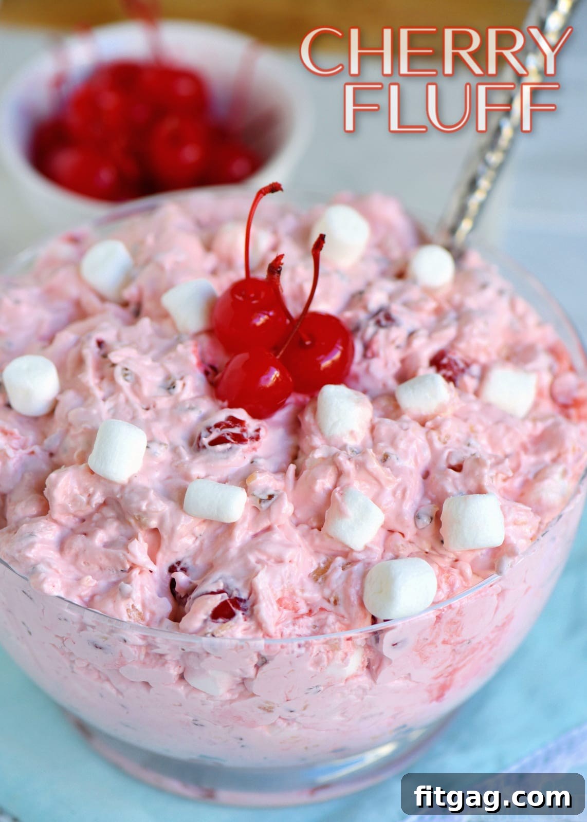Airy Cherry Delight 2 Cherry Fluff dessert salad served in a clear glass bowl with a spoon, showing its appealing pink color and creamy texture.