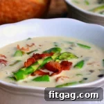 Close up of a bowl of creamy asparagus soup garnished with fresh herbs.