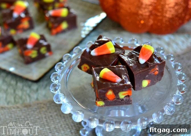Hand placing candy corn pieces onto warm, unset chocolate fudge to create an appealing pattern before chilling, highlighting a key step in fudge making.
