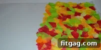 A section of waxed paper being covered with colorful tissue paper pieces, demonstrating the progress of the craft.