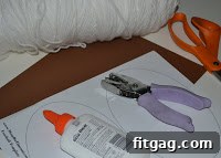 Essential crafting materials including glue, a hole punch, scissors, brown paper, and white yarn laid out on a clean counter